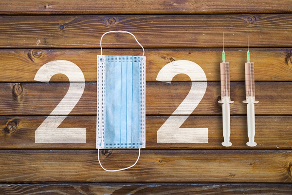 Masque bleu et seringues disposés pour représenter "2021" sur fond de bois, symbolisant l'année du coronavirus.