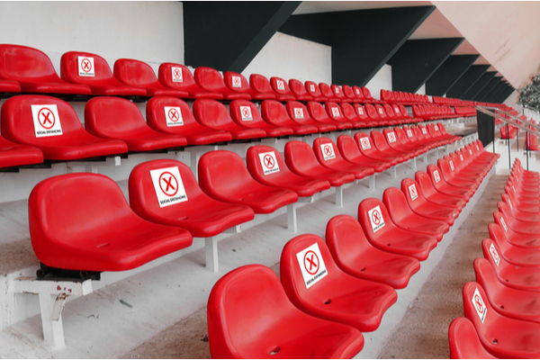 Sièges rouges dans un stade avec des panneaux interdisant l’utilisation de certains pour la distanciation sociale.