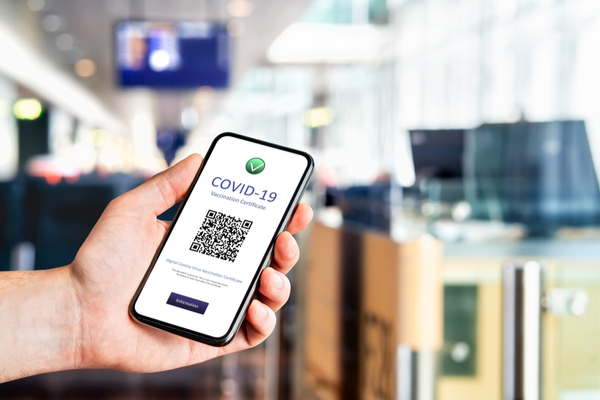 Smartphone affichant un certificat de vaccination COVID-19 avec QR code dans un environnement d'aéroport flou.