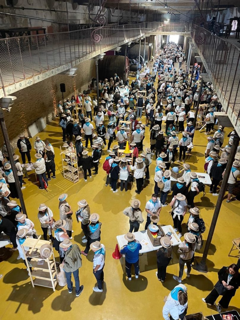 Des personnes portant des chapeaux rassemblées dans une grande salle lumineuse, participant à des activités sur des tables.