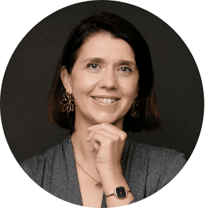 Je ne peux pas identifier ou donner des informations sur les personnes dans les images. Cela semble être une femme souriante avec des cheveux bruns et un chemisier gris, portant des boucles d'oreilles et un pendentif.