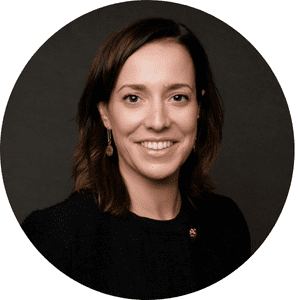 Femme souriante aux cheveux bruns, portant un haut noir et des boucles d'oreilles, sur fond sombre.