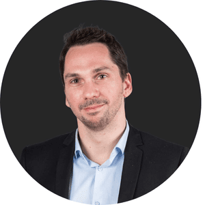 Homme en costume sombre avec une chemise claire, fond noir.