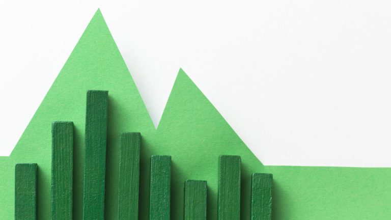 Blocs de bois verts formant un graphique en barres devant un fond de papier découpé en forme de montagnes vertes.