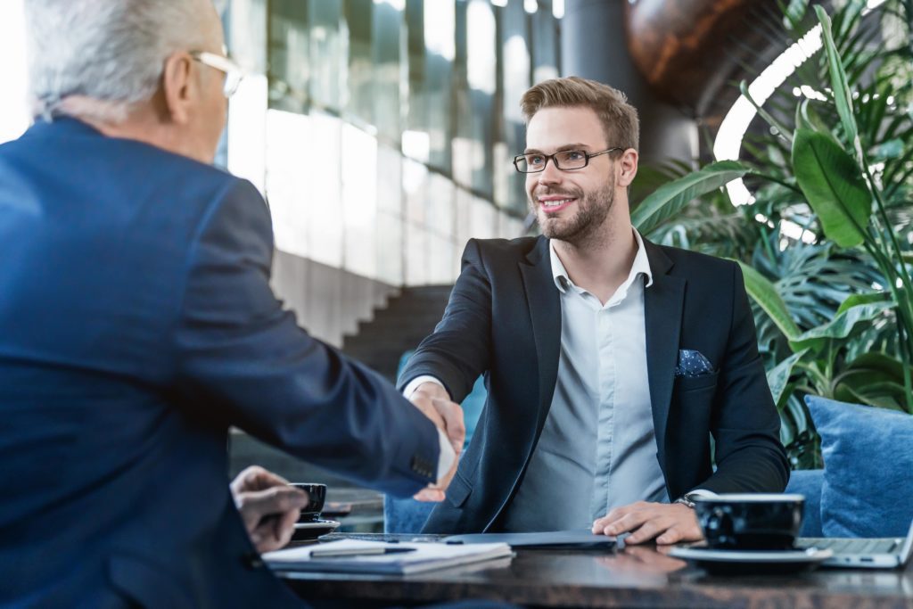 Deux hommes d'affaires se serrent la main dans un hall d'accueil moderne, entourés de plantes vertes.