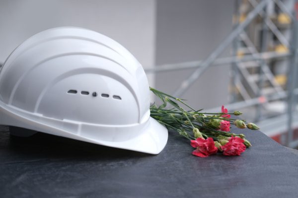 Casque de sécurité blanc posé à côté de fleurs rouges sur une table, symbolisant un accident de travail mortel.