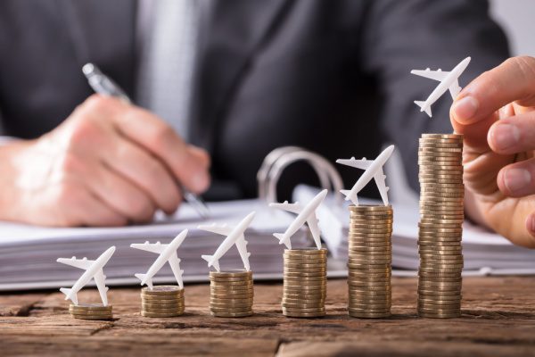 Avions miniatures sur des piles de pièces croissantes devant une personne écrivant, symbolisant la croissance financière.