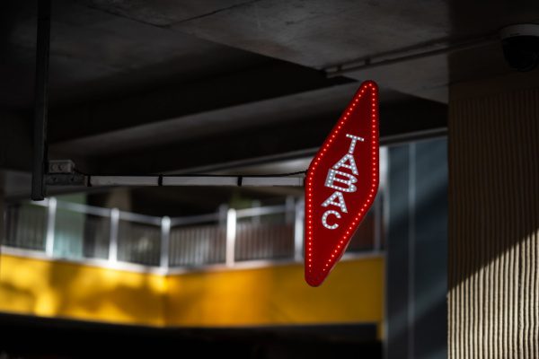 Enseigne lumineuse rouge en forme de losange avec l'inscription "TABAC", suspendue sous un plafond gris.