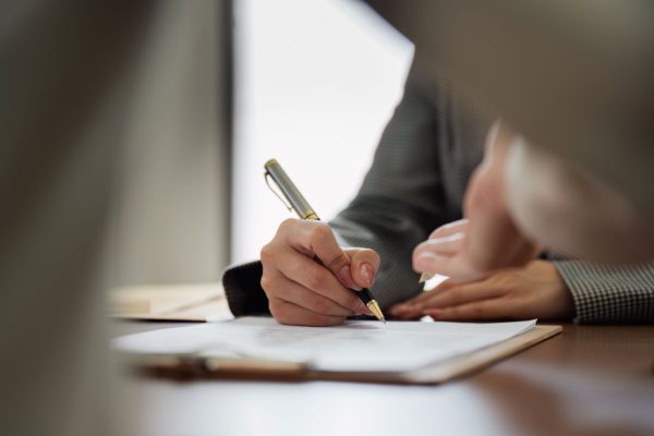 Main signant un document sur une table, suggérant la finalisation d'une convention ou contrat d'assurance.