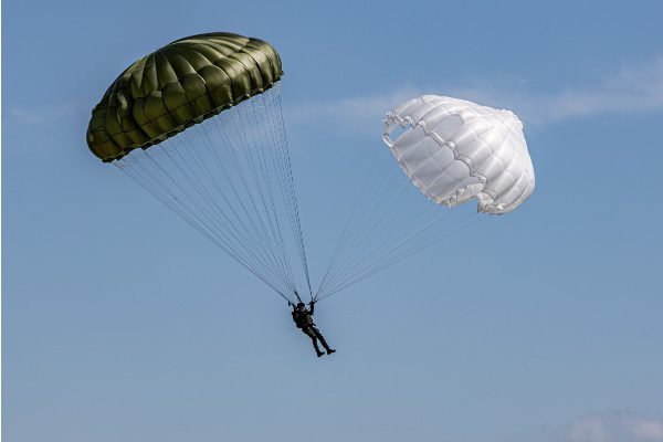 Parachutiste descendant avec un parachute vert et un blanc sous un ciel bleu clair.