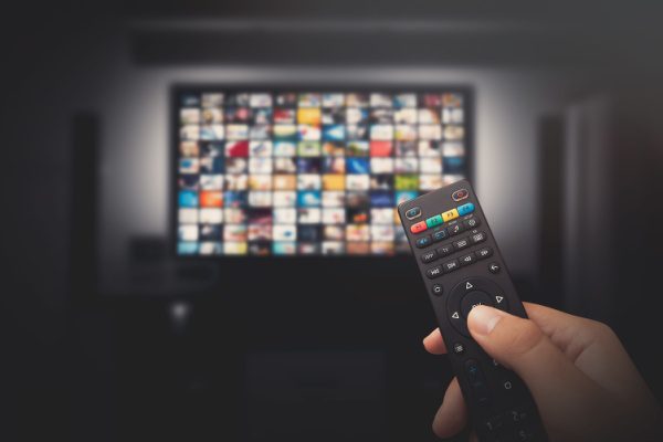 Télévision affichant un écran de sélection de services de streaming, avec une main tenant une télécommande au premier plan.