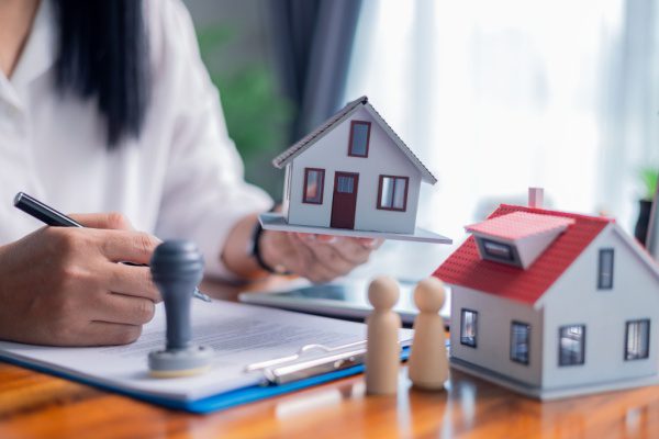 Personne signant des documents, tenant une miniature de maison, symbolisant l'achat immobilier.
