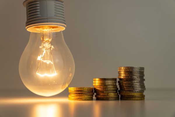 Ampoule allumée à côté de piles de pièces de monnaie, symbolisant la consommation et le coût de l'énergie.