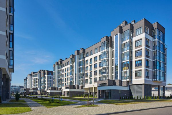 Immeubles d'appartements modernes avec façades vitrées et jardins bien entretenus sous un ciel bleu.