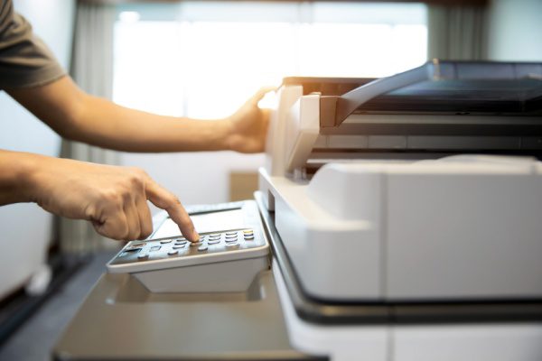 Personne utilisant une photocopieuse, appuyant sur un bouton du panneau de commande dans un bureau bien éclairé.