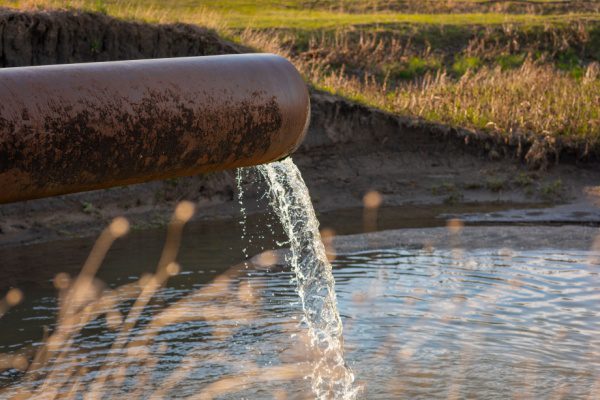 Eau s'écoulant d'un tuyau industriel rouillé dans un étang, évoquant la pollution par les PFAS dans l'environnement.