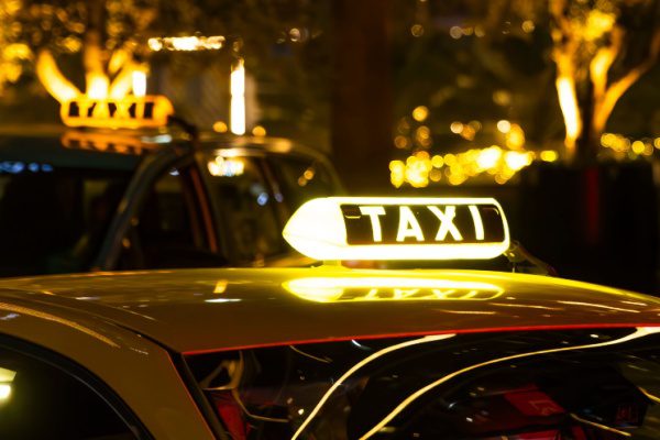 Taxi avec enseigne lumineuse jaune dans une rue éclairée nuit, ambiance urbaine et chaleureuse en arrière-plan.