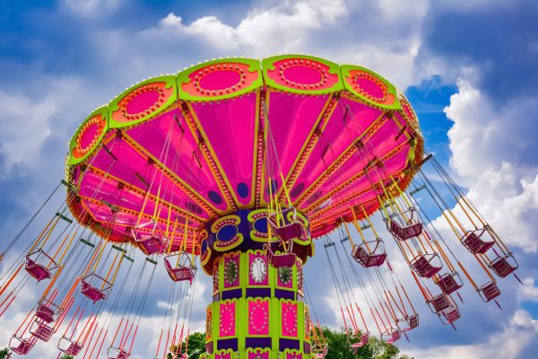 Carrousel démontable aux couleurs vives avec des sièges suspendus, se détachant sur un ciel nuageux.