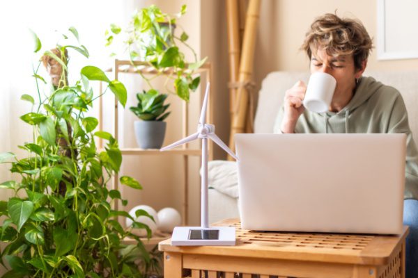 Personne buvant une boisson chaude devant un ordinateur portable, entourée de plantes, symbolisant le télétravail écologique.